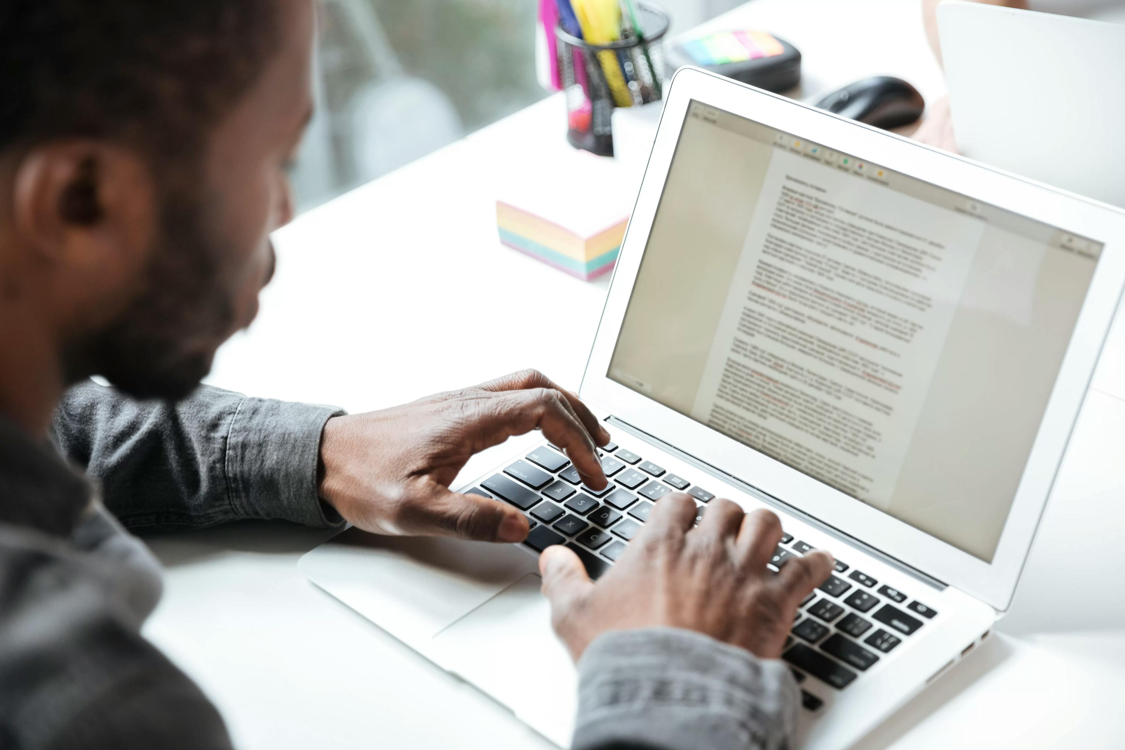 Homem digitando em um notebook em um ambiente de escritório, com foco na tela que exibe um documento de texto. A imagem transmite a ideia de trabalho, escrita e produção de conteúdo, possivelmente relacionado a copywriting ou tarefas de escritório.