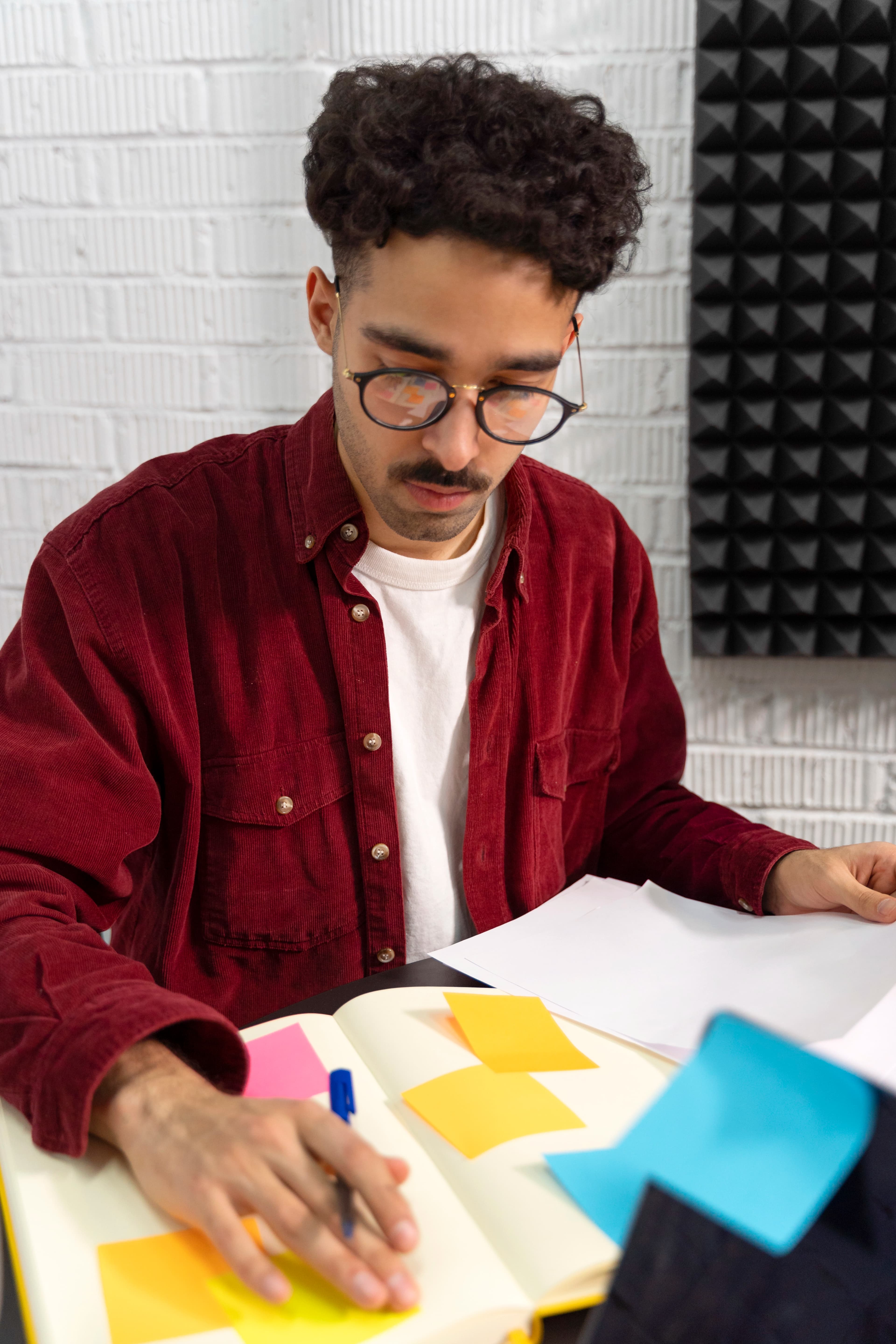 Homem vestindo uma camisa bordô e está usando óculos. Está no processo de Criação e Planejamento de Conteúdo